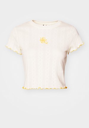 Īsu piedurkņu balta t-kreklu, ribota tekstūra, ar dzeltenām frillēm un ziedu izšuvumu centrā uz krūškurvja.