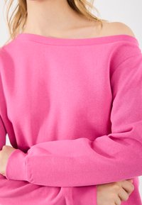 Rosa averskjorte med lange ermer, laget av mykt stoff. Har ribbestrikket halslinning og mansjetter, og viser en avslappet passform.