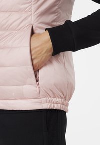 Růžová péřová vesta s prošívanou texturou, zipovými kapsami a elastickým lemem. Černý rukáv s žebrovaným manžetem. Lehký, pohodlný design.