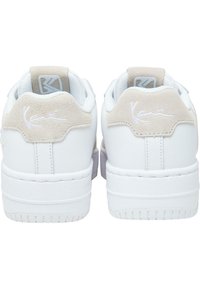 Sneakers bianchi con tomaia in pelle liscia e accento in morbida pelle scamosciata sul tallone. Presentano un logo distintivo e suola in gomma texturizzata. Design minimalista.