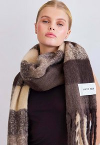 Gebreide wolscarf in een ruitpatroon met tinten bruin en crème. Label met de tekst "ARCTIC FOX". Franje aan de randen voor extra textuur.