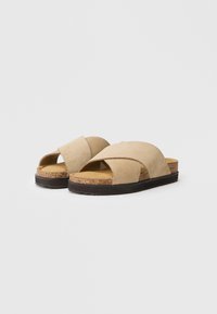 Sandali slides in suede beige con cinturini a punto croce, soletta in sughero e suola in gomma nera, caratterizzati da un design aperto davanti e senza retro.