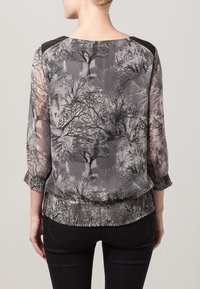 Przezroczysta czarna i szara bluzka z wzorem przypominającym gałęzie, z rękawami o długości trzech-czwartych i marszczonym dołem. Czarne akcenty na ramionach.