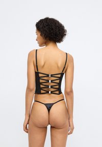 Conjunto de lencería negra que incluye un corsé ajustado con un respaldo de encaje y acentos metálicos, combinado con un tanga a juego. Tejido suave y elegante.