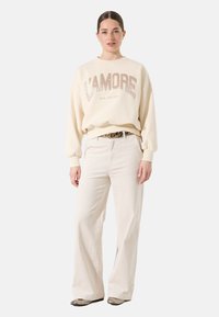 Sudadera off-white con gráfico "L'AMORE" en beige, combinada con pantalones de pana beige claro. Tejido suave y corte relajado.