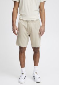 Shorts de ocio de algodón beige con cintura elástica y cordón. Combinados con una camiseta a juego y detalles en zapatillas blancas.