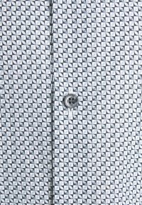 Bouton gris sur tissu avec un motif géométrique répétitif de quartiers de cercles blancs, noirs et gris formant des carrés.