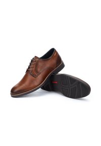 Chaussures derby en cuir marron avec lacets, bout arrondi, intérieur contrastant bleu marine et semelle extérieure en caoutchouc noir texturé avec reliefs.