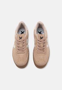 Zapatillas de ante beige con punta redonda, superficie texturizada, detalles en crema y suelas gruesas de goma. Cordones y logotipo en negro.