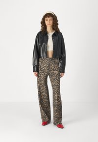 Svart kort læderjakke, cremet kort top, beige leopardmønstrede brede bukser, røde hæle; model med krøllet hår iført et hårbånd.