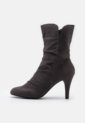 Botte mi-mollet en daim gris foncé avec bout pointu, détails froncés, fermeture éclair latérale et talon aigu élégant sur fond blanc.