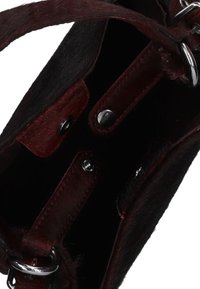 Zwarte en bordeauxrode tas met een vachttextuur, metalen accessoires en drukknoopsluitingen. Het interieur is donker en niet versierd met leren banden.