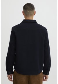 Navy blue, long-sleeve shirt with a collar, buttoned cuffs, and a straight hem. Made of soft fabric, showcasing minimalistic design.
