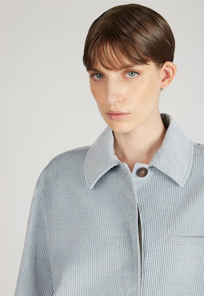 Jasnoniebieska kurtka koszulowa z korduroy, z szerokim kołnierzem, zapięciem na jeden guzik oraz detalem kieszeni na piersi, z pionowymi paskami.