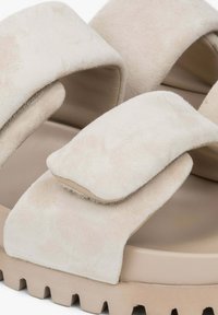 Beige suede sandals with wide, adjustable straps and a thick, textured sole featuring ridged detailing. Soft surface and minimalist design.