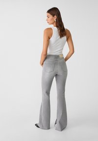 Jeans grijs évasés avec une taille mi-haute, comportant des poches arrière et une étiquette de marque discrète au niveau de la ceinture. Texture en denim lisse.
