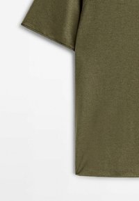 Tissu vert olive à manches courtes avec surpiqûres visibles à l'ourlet, présenté sur fond blanc, montrant la partie supérieure du torse.