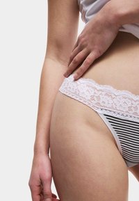 Nahaufnahme einer Person, die ihre schwarz-weiß gestreifte Unterwäsche mit weißer Spitzenborte an der Hüfte vor einem schlichten Hintergrund anpasst.