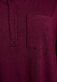 Burgundská košeľa s textúrovanou tkaninou, gombíkovou henley krčnou líniou a jedným náprsním vreckom. Obsahuje detail kontrastného šitia.