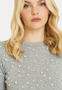 Szary sweter z okrągłym dekoltem, zdobiony perłami i przezroczystymi kamieniami rozmieszczonymi na tkaninie, charakteryzujący się miękką dzianiną.