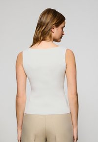 Top entallado sin mangas en tejido de canalé gris claro, con escote cuadrado y espalda sin costuras, combinado con pantalones beige.