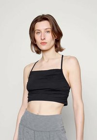 Top preto cropped com alças finas, apresentando textura franzida e decote quadrado. Tecido liso sem padrões, combinado com partes inferiores cinzentas.