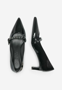 Escarpins noirs en cuir verni à bout pointu avec une lanière de cheville ornée d'œillets en argent, présentés en vue de dessus et de côté sur un fond blanc.