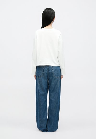 Biała bluzka z długim rękawem i zaokrąglonym dekoltem, zestawiona z szerokimi, dżinsowymi spodniami w kolorze niebieskim, wyposażonymi w dwie tylne kieszenie i luźny krój.