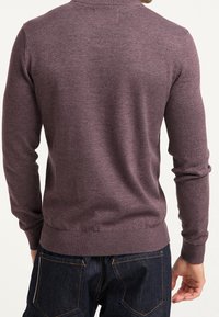 Sweter w kolorze ciemnego mauve, wykonany z miękkiego dzianiny. Ma długie rękawy i dopasowany dół, noszony na ciemnych dżinsach.