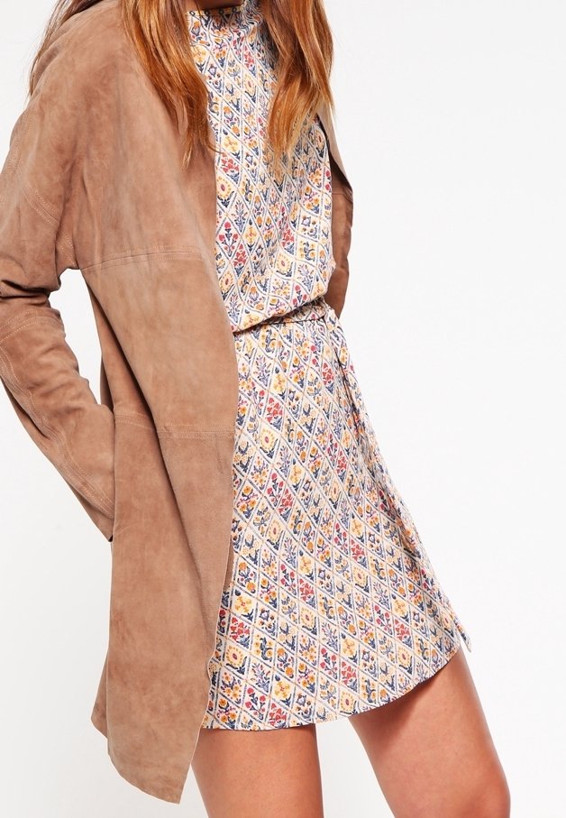 Südsbrun jacka som är lagd över en mönstrad klänning med ett diamantmönster i blått, gult och rött på en ljus bakgrund.