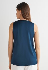 Marinblå ärmlös topp i silkesliknande material, med rundad halsringning och sprund i nederkanten för ökad rörelsefrihet.