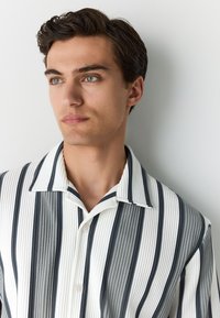 Gestreept shirt met korte mouwen in wit, grijs en marineblauw. Heeft een verticale geribbelde textuur en een puntige kraag met twee knopen.