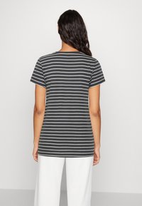 Camiseta de rayas blancas y negras de manga corta, material suave de algodón, con cuello redondo y un ajuste relajado, vista desde la parte posterior.