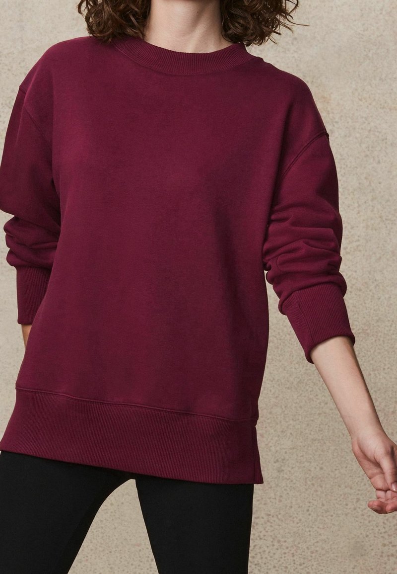 Bordeaux Sweatshirt aus weichem Stoff mit Rundhalsausschnitt, überschnittenen Schultern, gerippten Bündchen und einem lockeren Schnitt mit einem etwas längeren Rücken.
