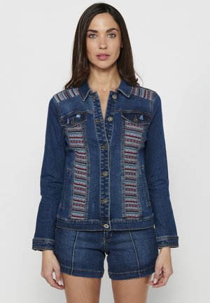 Denim-takki, jossa on monivärisiä kudottuja yksityiskohtia harteilla, nappikiinnitys, kaksi etutaskua ja vartalonmyötäinen muotoilu.