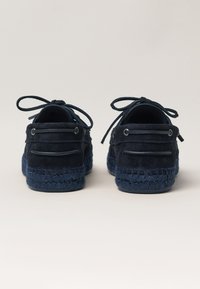 Zapatos de ante azul marino con suela de esparto texturizada, puntera redonda y diseño de cordones. Presentan detalles de costura y ojales para los cordones.