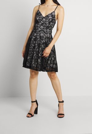 Czarna koronkowa sukienka z dopasowanym gorsetem, dekoltem w szpic i rozkloszowanym dołem. Złożona z misternych wzorów paisley. Dobrana z czarnymi sandałami na paski.
