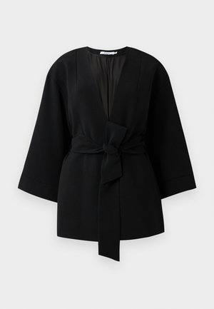 Černý kimono stylový kabát s dlouhými rukávy a širokými manžetami, s předním látkovým páskem svázaným uzlem v pase.