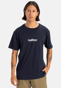 Camiseta de algodón azul marino con un logotipo blanco de Quiksilver en el centro. Diseño de mangas cortas y cuello redondo. Textura suave.