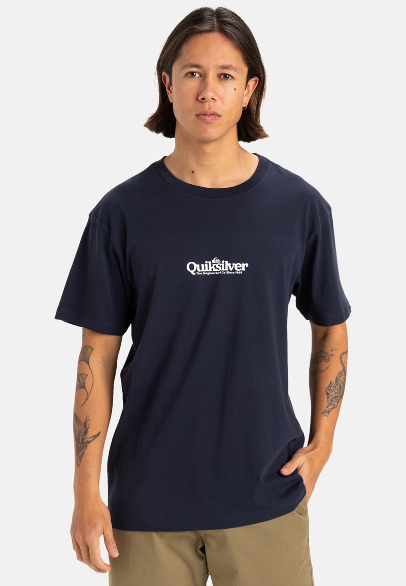 Camiseta de algodón azul marino con un logotipo blanco de Quiksilver en el centro. Diseño de mangas cortas y cuello redondo. Textura suave.