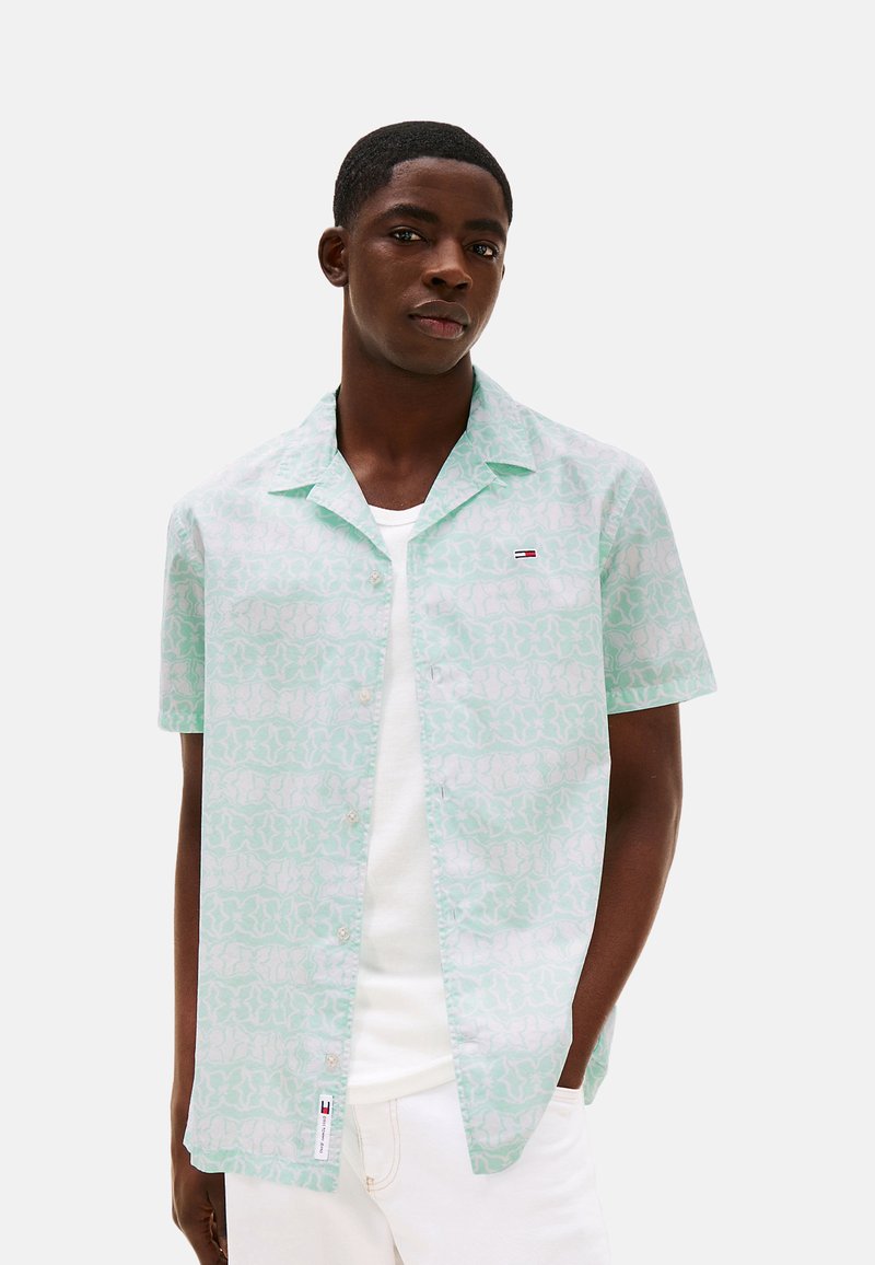 Camisa de manga corta en color verde menta con un ligero patrón abstracto, con cierre de botones en la parte delantera y un pequeño logo en el pecho. Tejido de algodón, corte relajado.