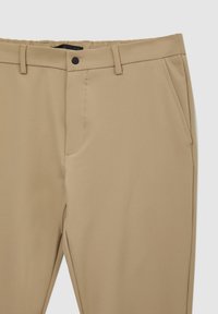 Pantaloni beige realizzati in tessuto liscio, dotati di una parte anteriore piatta, tasche laterali e una vita con chiusura a un solo bottone.