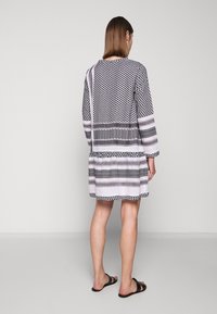 Vestido de estampado en blanco y negro con diseños geométricos y rayas horizontales. Manga larga, cae a mitad del muslo, tejido ligero.