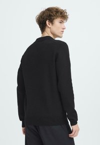 Čierny pletený sveter s okrúhlym výstrihom, dlhými rukávmi a rebrovaným prrúžkom. Textúra vyzerá mäkko a husté.