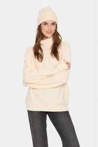 Suéter de cuello alto crema con un corte holgado, puños acanalados, combinado con un gorro a juego. Textura suave, tela ligera, apariencia lisa.