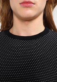 Maglione nero in maglia con un motivo testurizzato bianco. Caratterizzato da un colletto rotondo a coste e una vestibilità aderente.