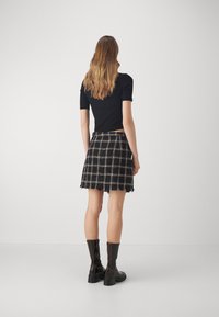 Sort ribbet bluse med korte ærmer, parret med en ternet mini-skjorte med franskede kanter. Modellen har knæhøje sorte støvler med lynlås på.