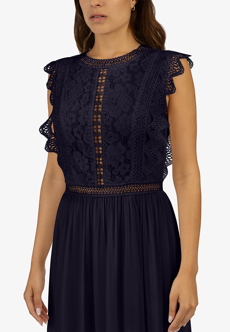 Robe marine avec un haut en dentelle délicate présentant des manches à volants, des motifs floraux et une taille texturée, s'épanouissant en une jupe lisse et froncée.