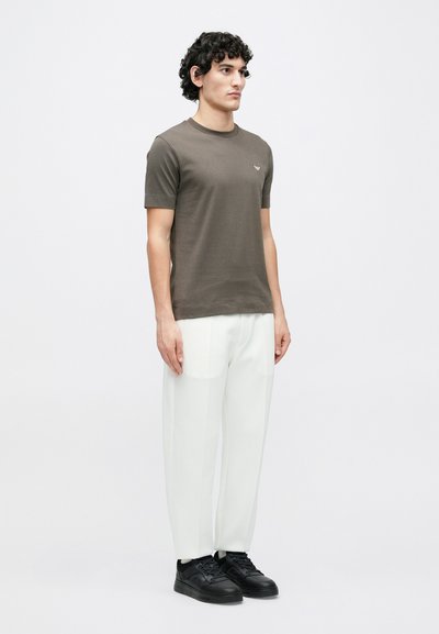 Tmavozelené tričko s krátkym rukávom a okrúhlym výstrihom, nosené s bielymi obdĺžnikovými nohavicami a čiernymi teniskami. Minimalistický dizajn, bez vzorov.