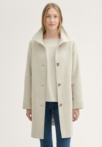 Bézs gyapjú keverék kabát széles gallérral, elülső gombokkal és vízszintes varrási részletekkel a belső rétegen, csíkos inggel párosítva.